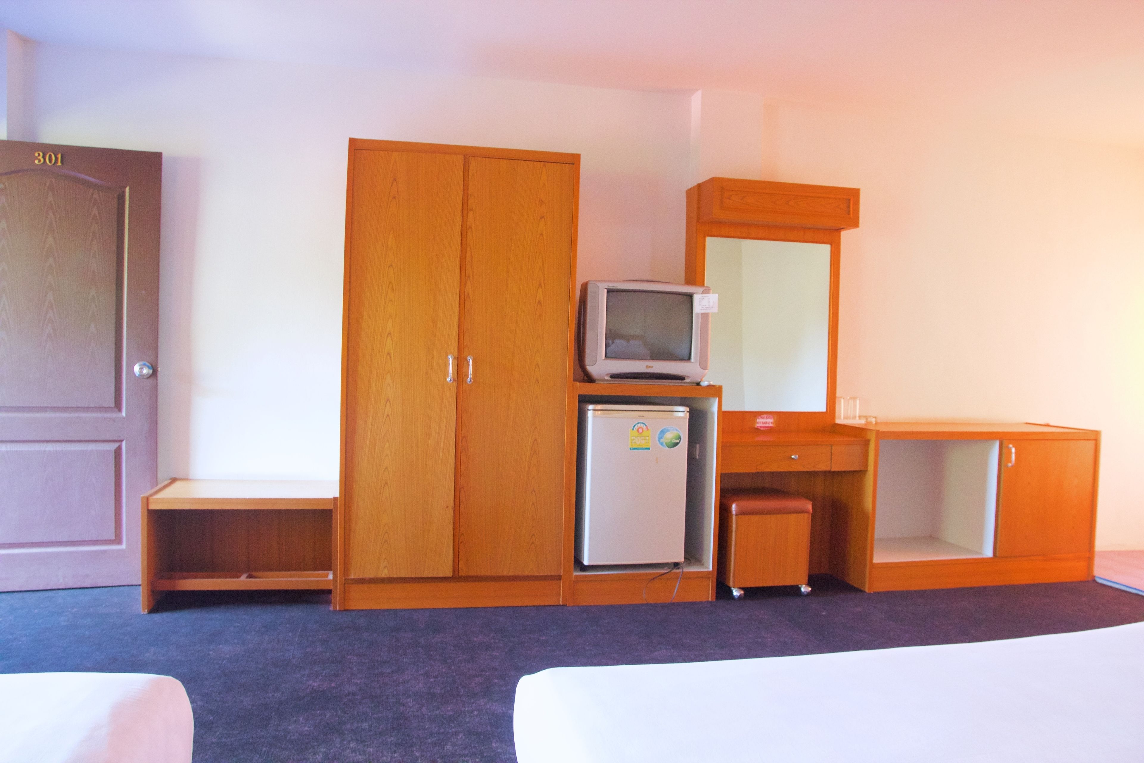 Une chambre d’hôtel équipée d’une armoire en bois, d’un petit réfrigérateur, d’une télévision et d’un bureau.