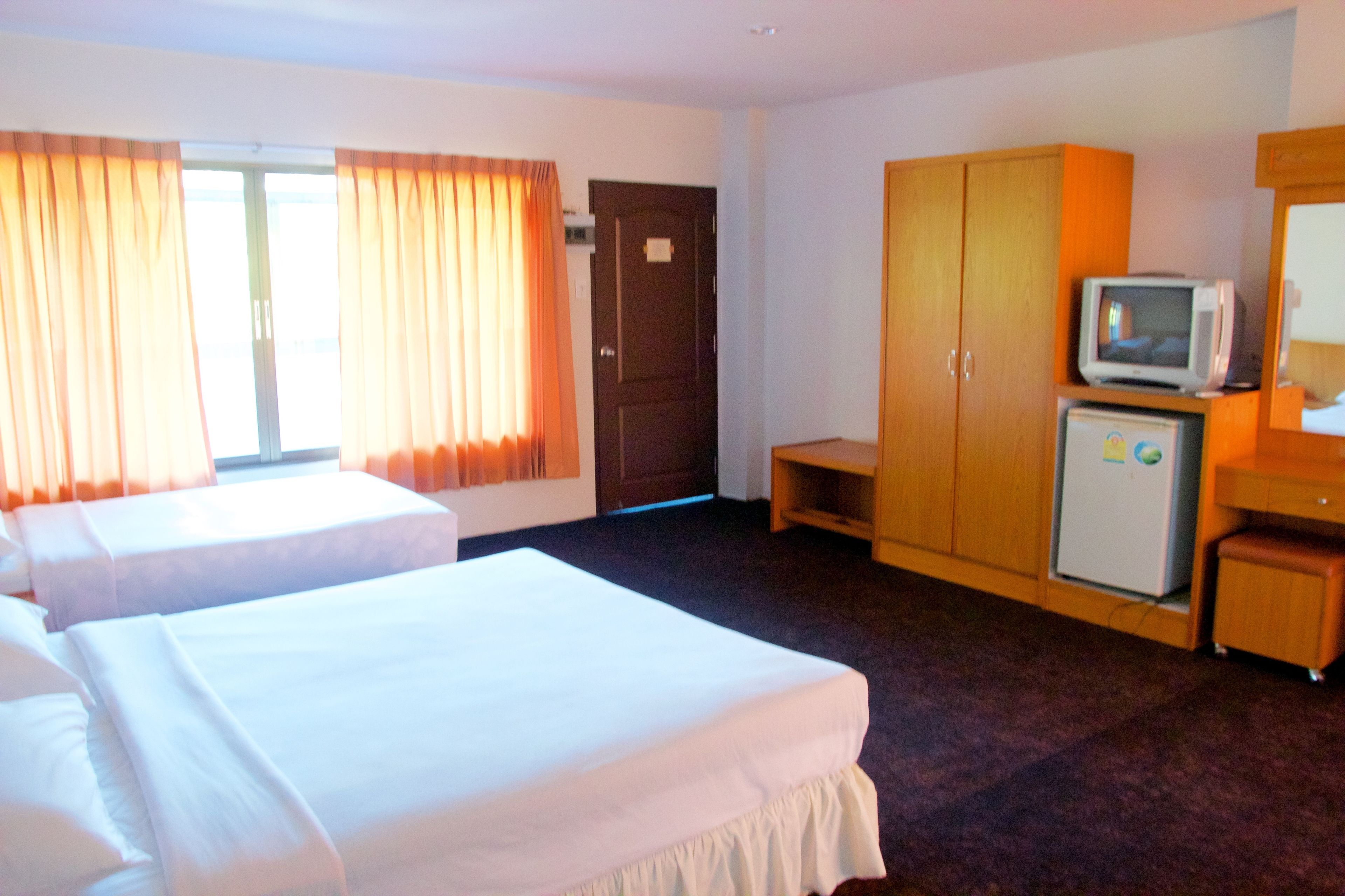 A hotel room with two beds, a television, a refrigerator, and a wardrobe.