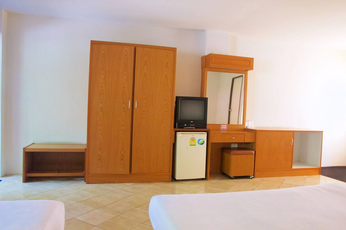 Une chambre d’hôtel avec une armoire en bois, un petit réfrigérateur, une télévision, un bureau et un lit.