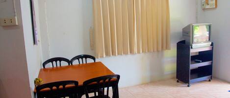 A dining area with a wooden table and four chairs, a window with beige curtains, and a television on a stand.