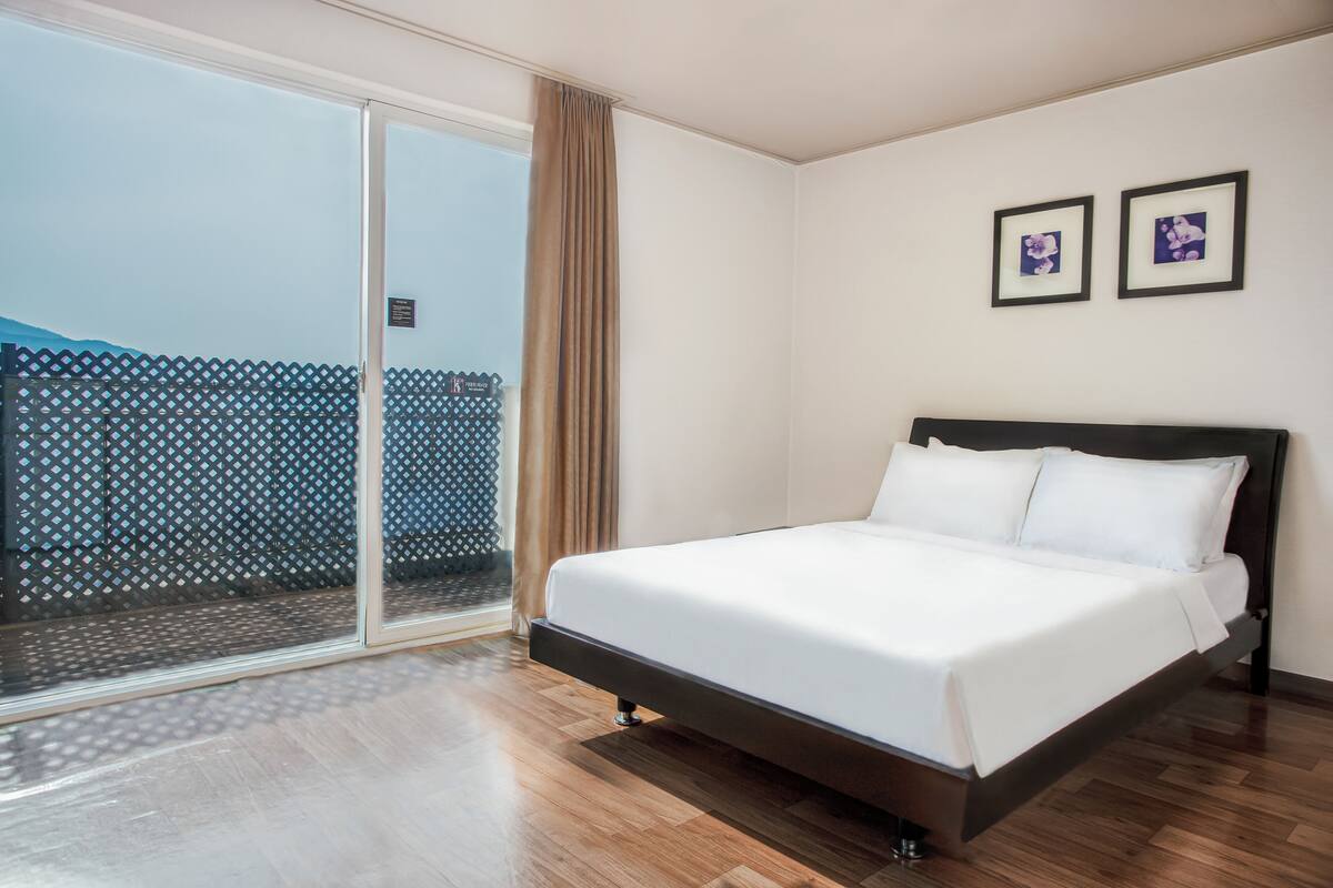 Een hotelkamer met een groot bed, een schuifglazen deur naar een balkon en twee ingelijste foto’s aan de muur.