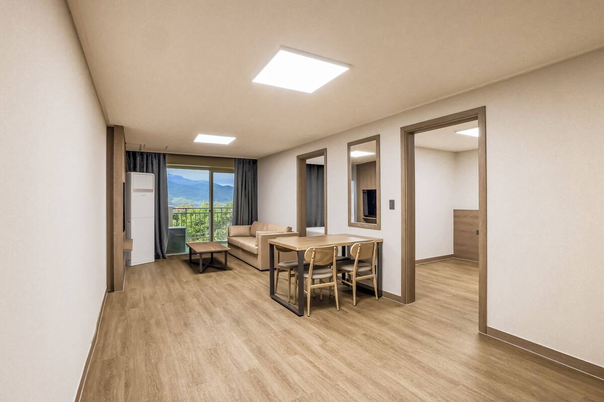 Een ruime kamer met houten vloer, een eettafel met stoelen, een bank en een groot raam met uitzicht op bergen.