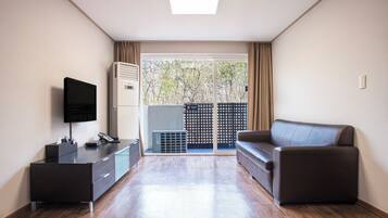 Una sala de estar moderna con un televisor de pantalla plana, un sofá oscuro, piso de madera y un puerta corrediza de vidrio que da a un espacio exterior.