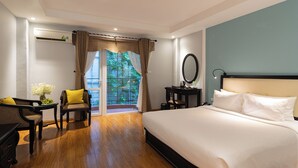 A hotel room with a large bed, a desk with a chair, a small table with a vase of flowers, and a view of a garden through a glass door. - Hoian Sincerity Hotel & Spa (Da Nang)