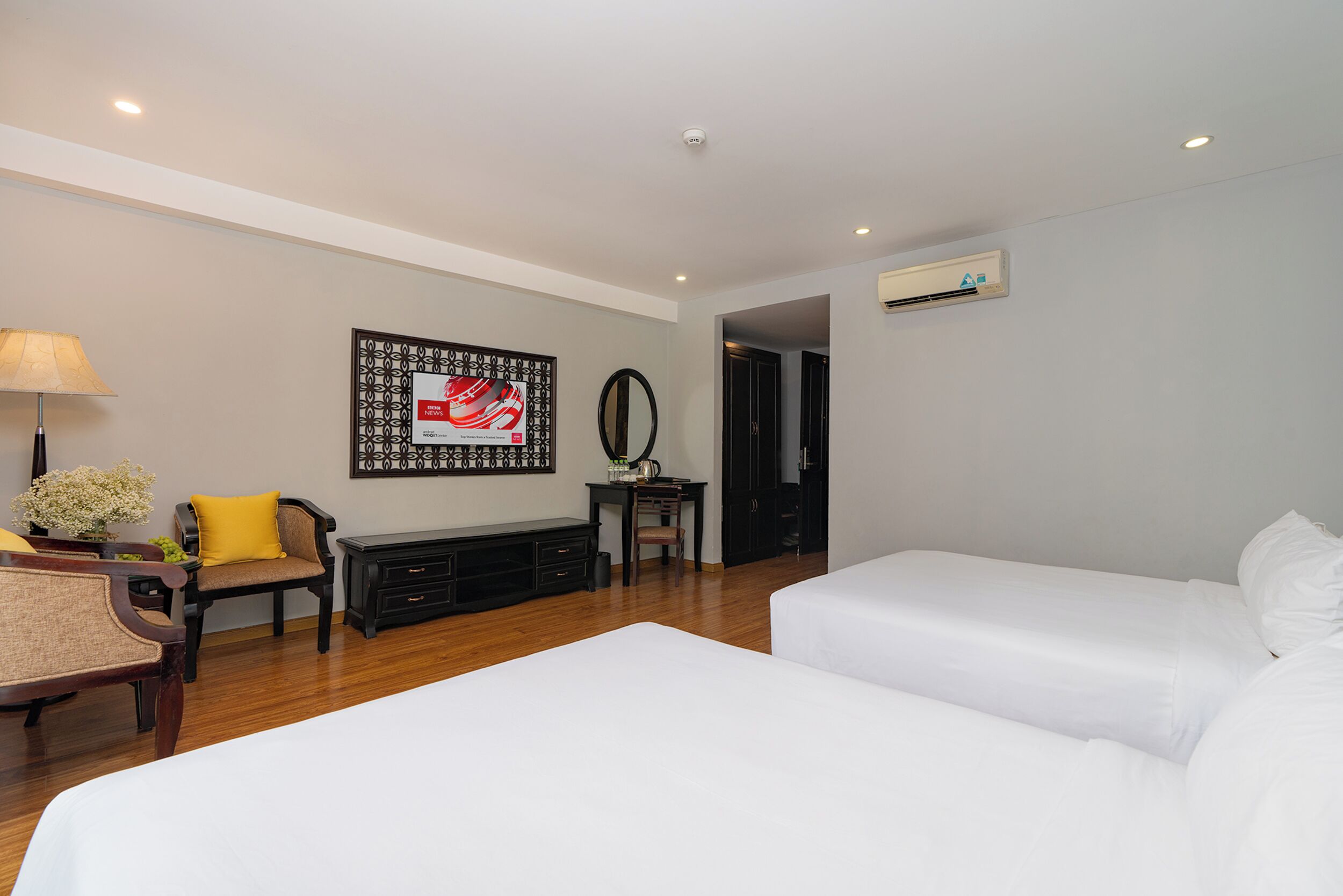 Ein Hotelzimmer mit zwei Betten, einem Schreibtisch mit Stuhl, einer Lampe und einem gerahmten Bild an der Wand.
