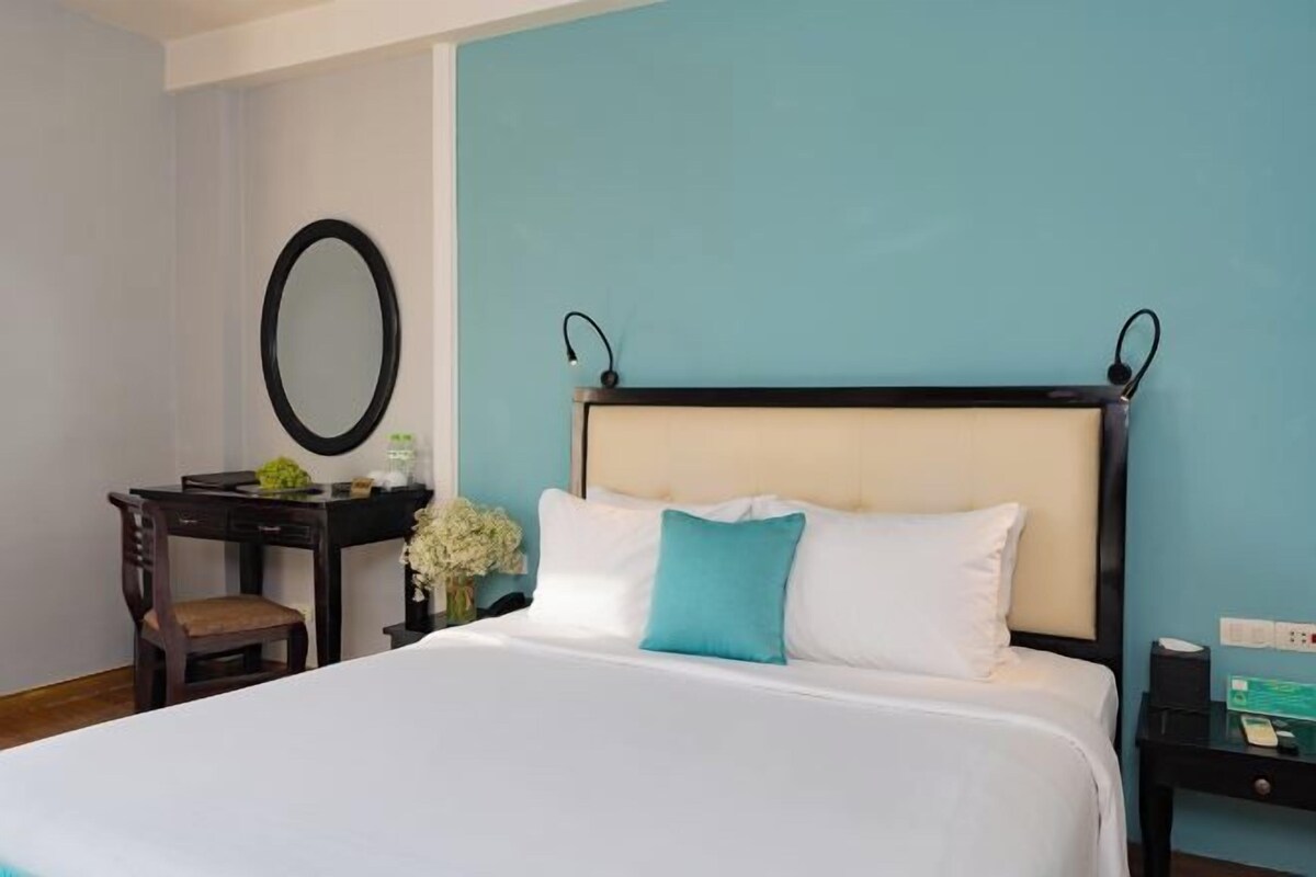 A hotel room with a bed, a desk, a chair, a mirror, and a nightstand.