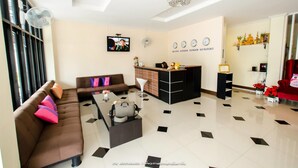A modern living room with a sofa, coffee table, and a TV. There is a reception desk and a chandelier. - Petch Ranong at Town (Ranong)