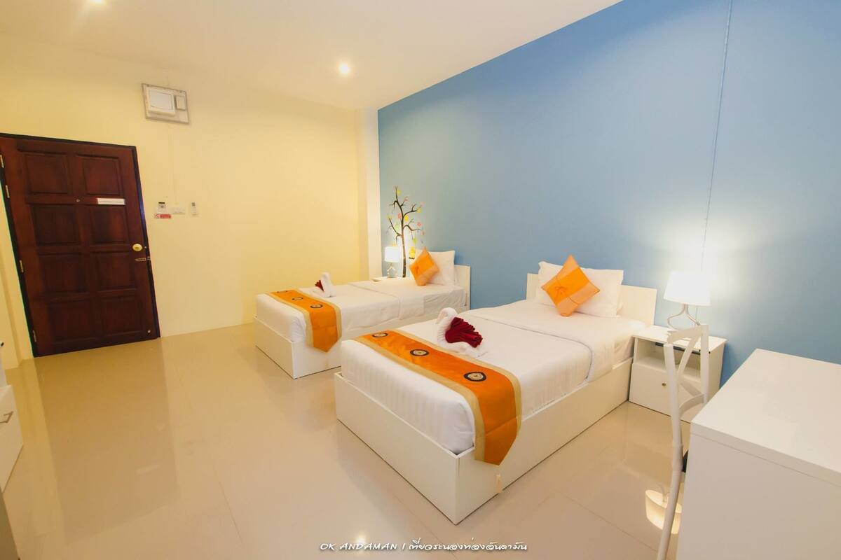 A hotel room with two beds, a wooden door, a white nightstand with a lamp, and a blue accent wall.