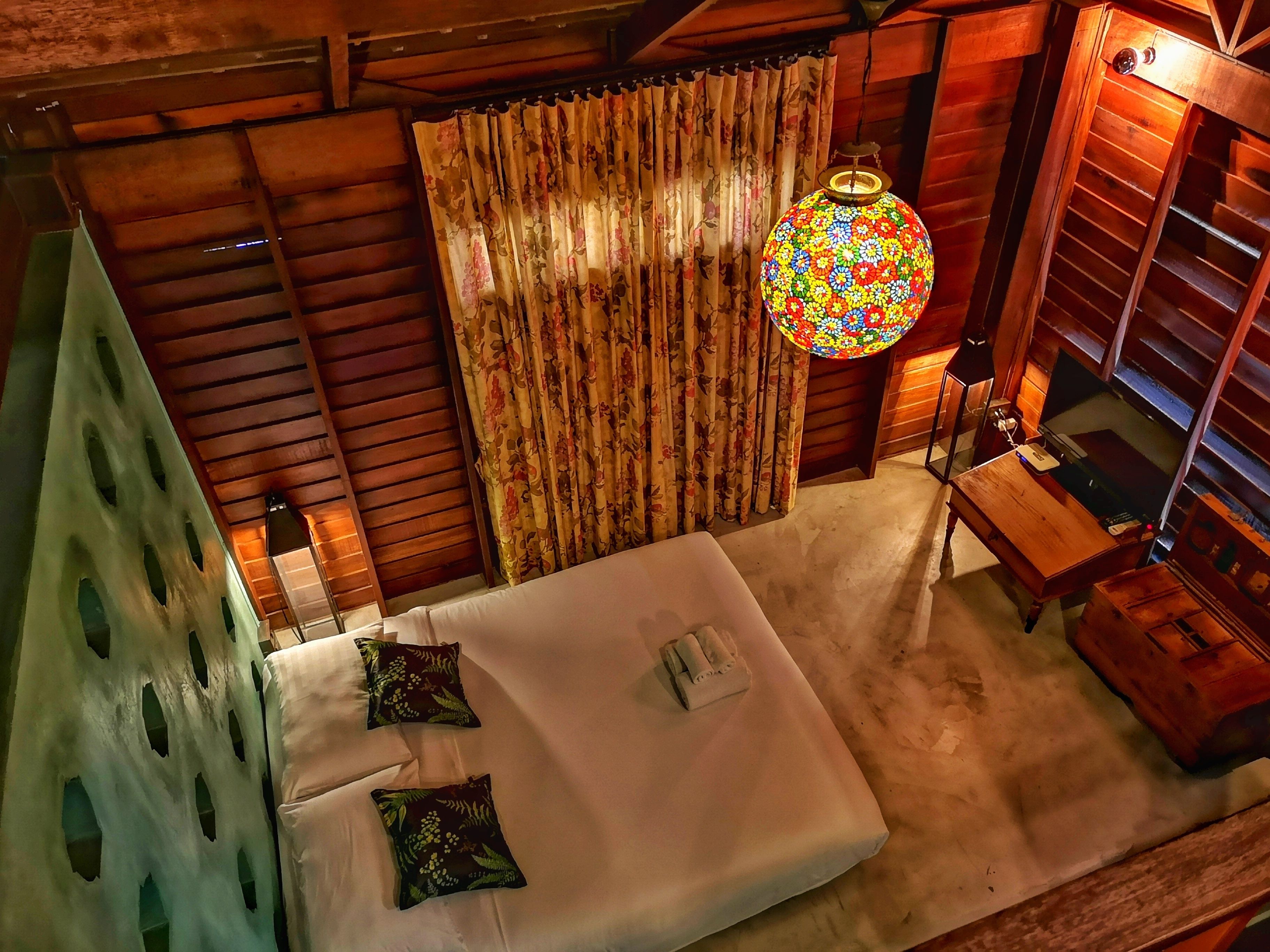 A room with a bed, a wooden ceiling, a curtain, and a hanging lamp.