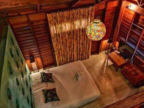 A room with a bed, a wooden ceiling, a curtain, and a hanging lamp.