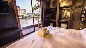 Une chambre d’hôtel avec un lit, une fenêtre donnant sur une rivière et des bâtiments, et des étagères en bois sur lesquelles sont posés divers objets.