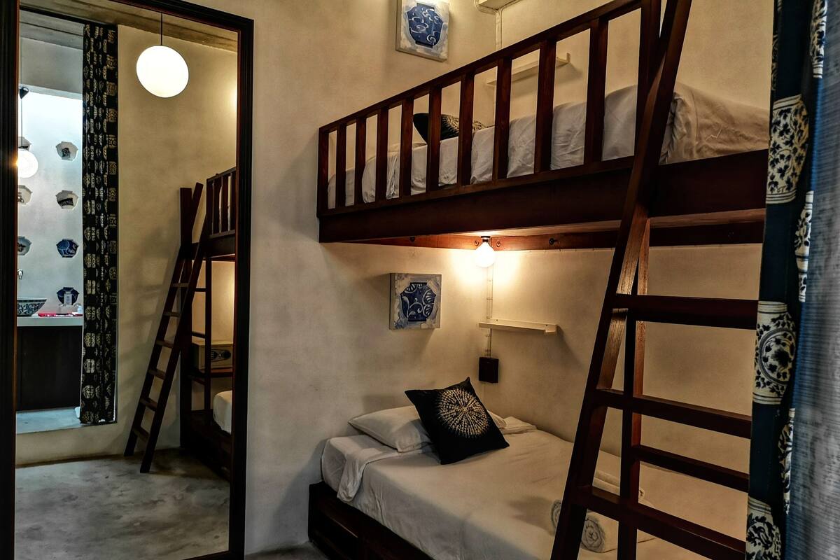Een slaapkamer met een stapelbed, een nachtkastje, een wandlamp en een spiegel.