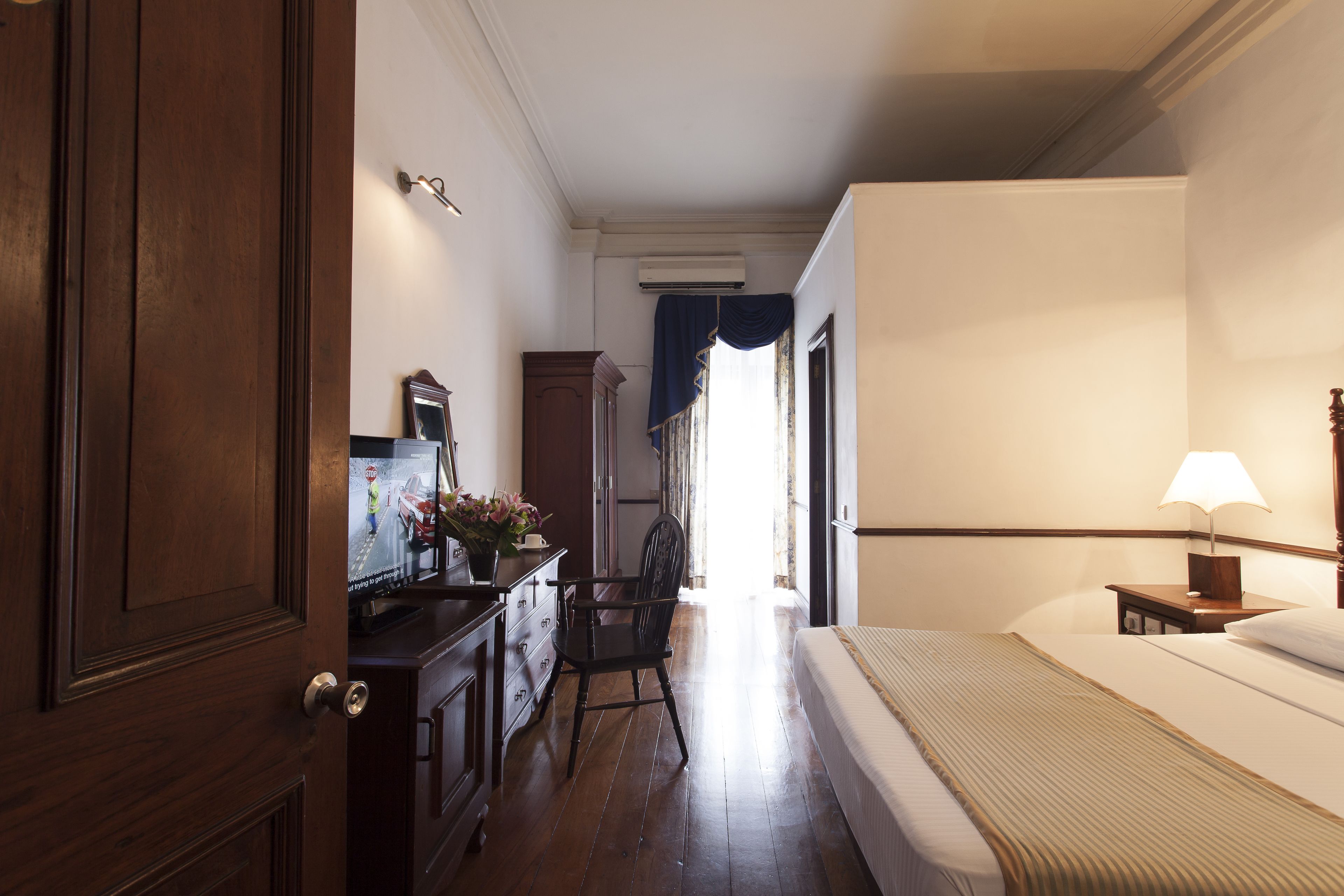 Een hotelkamer met een bed, een bureau met lamp, een stoel en een dressoir.