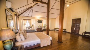A spacious room with a large bed, wooden flooring, a sitting area with chairs, a television, and a door. - Queen's Hotel (Kandy)