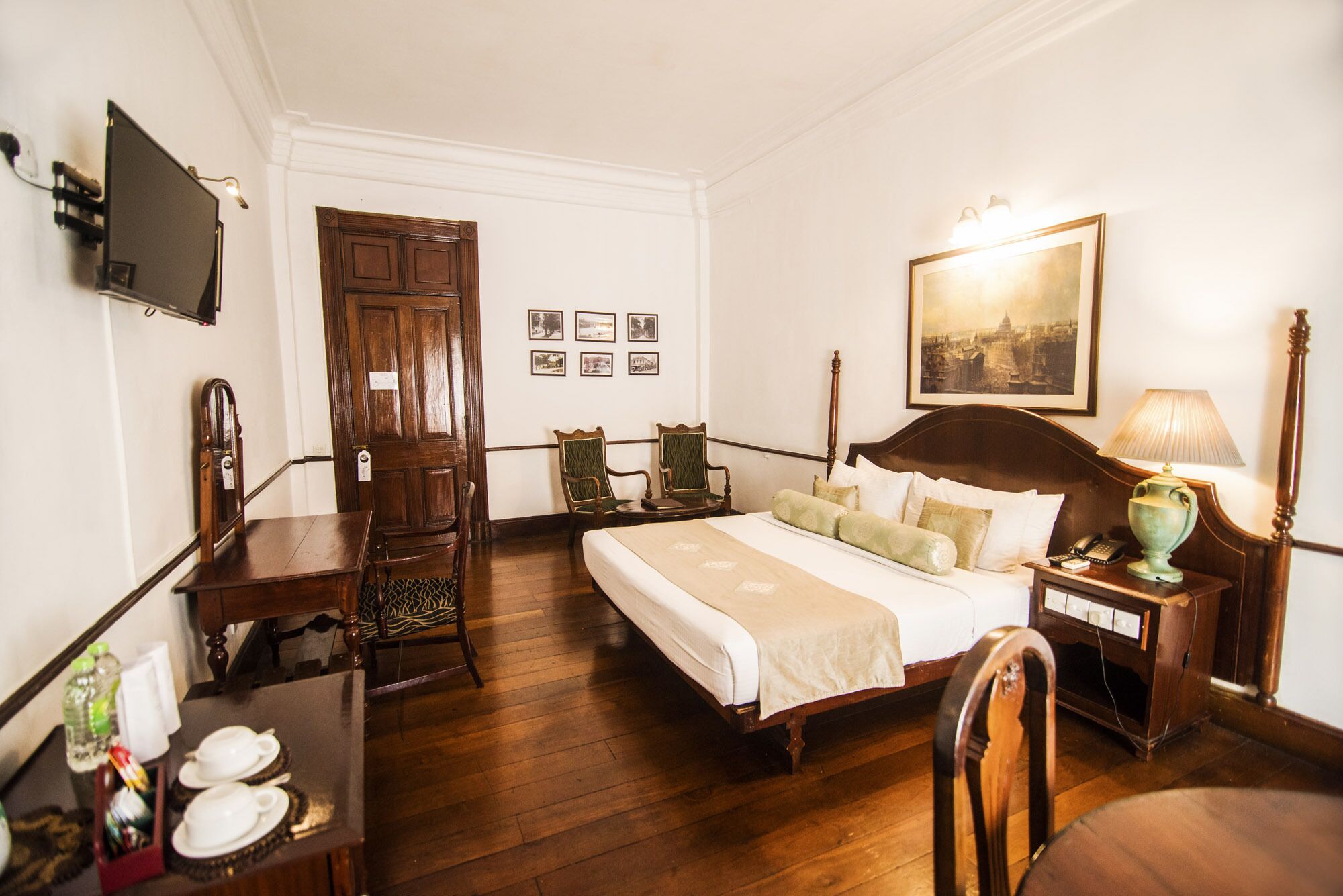 Une chambre d’hôtel avec un lit en bois, un bureau avec une chaise, une télévision et un tableau au mur.