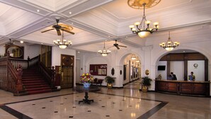 A grand lobby with a marble floor, a central floral arrangement, a reception desk, and a staircase with a wooden railing. - Queen's Hotel (Kandy)