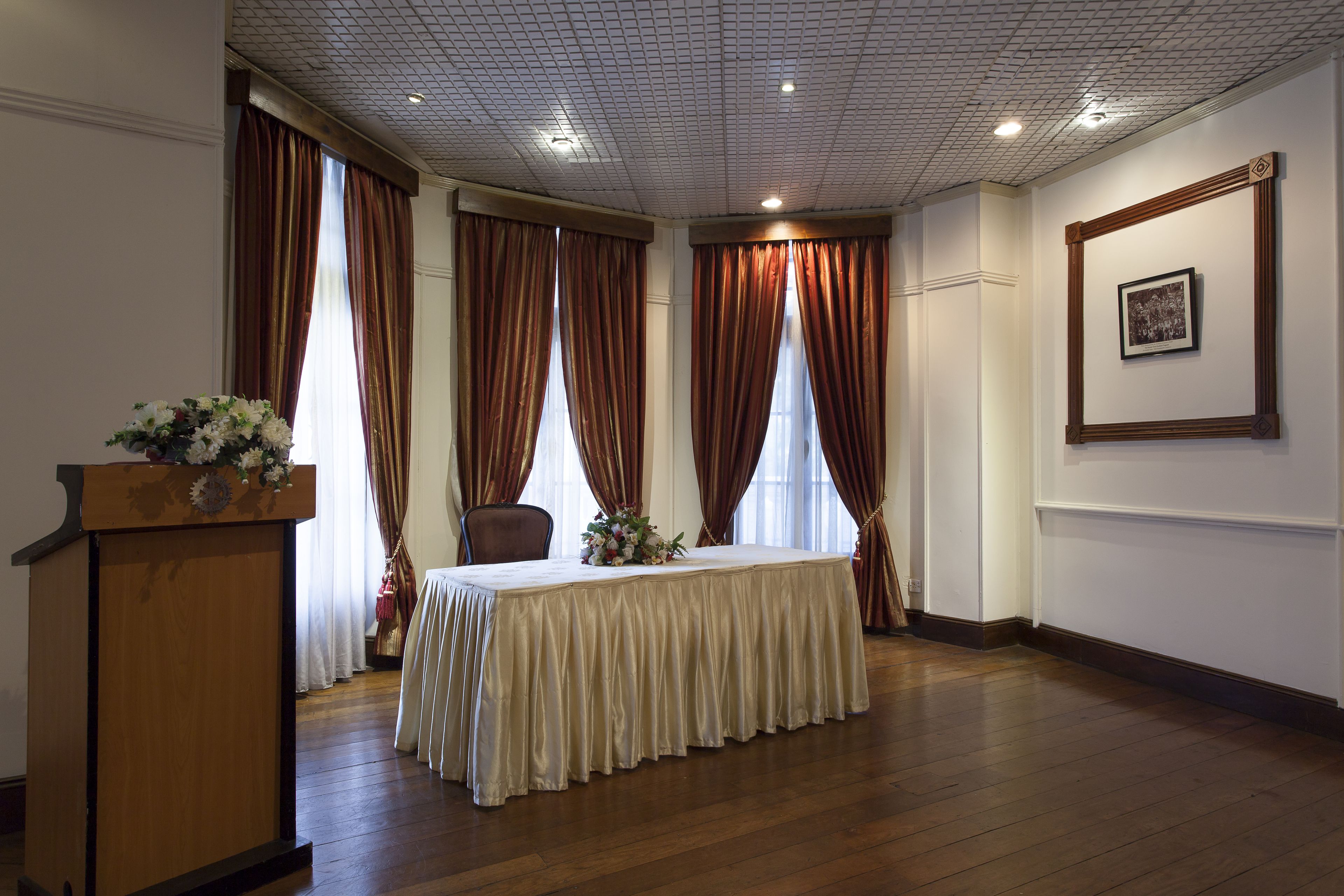 A room with a wooden podium, a table with a draped tablecloth, and a framed picture on the wall.