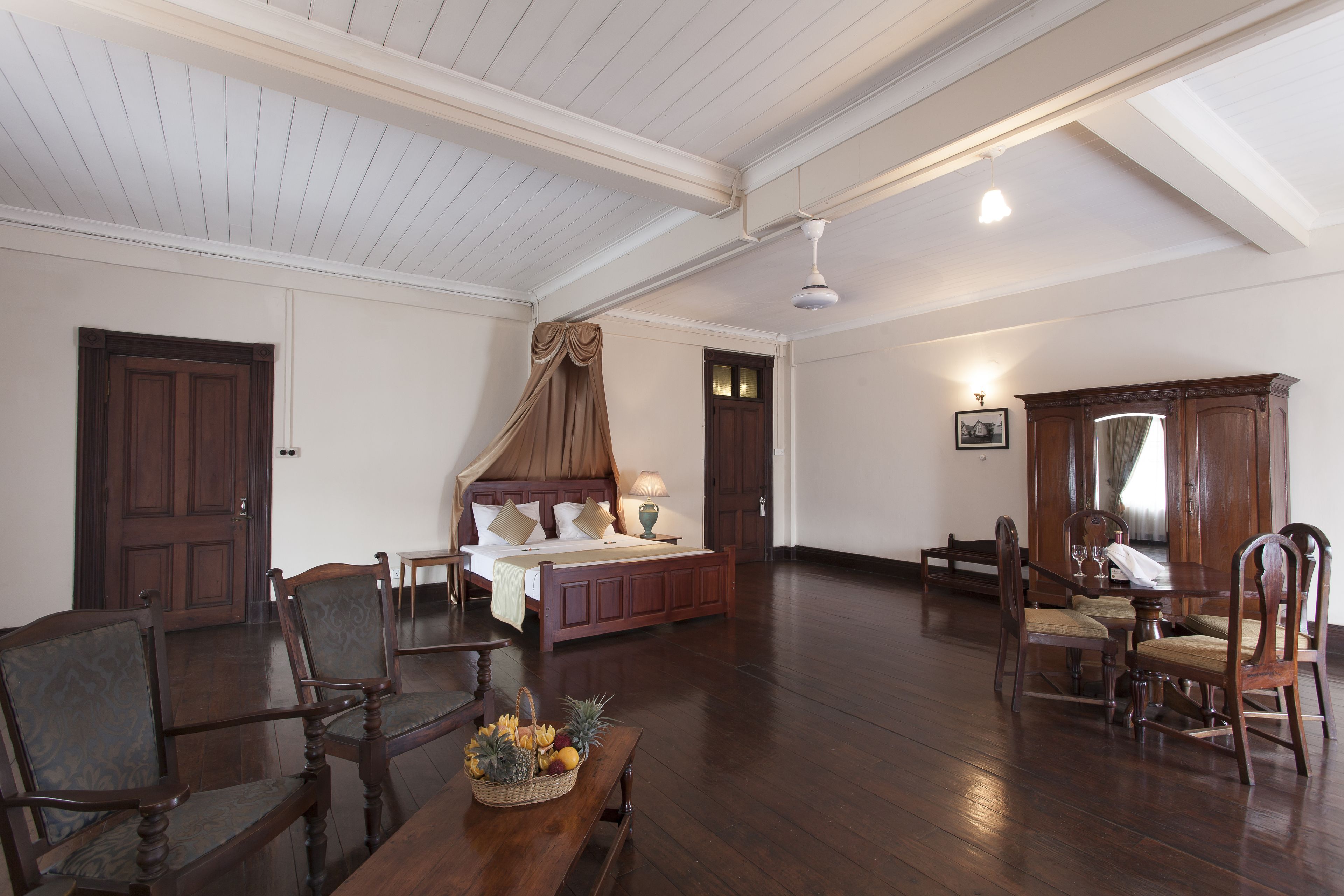 Una habitación amplia con una cama grande, una mesa de comedor con sillas y un armario de madera.
