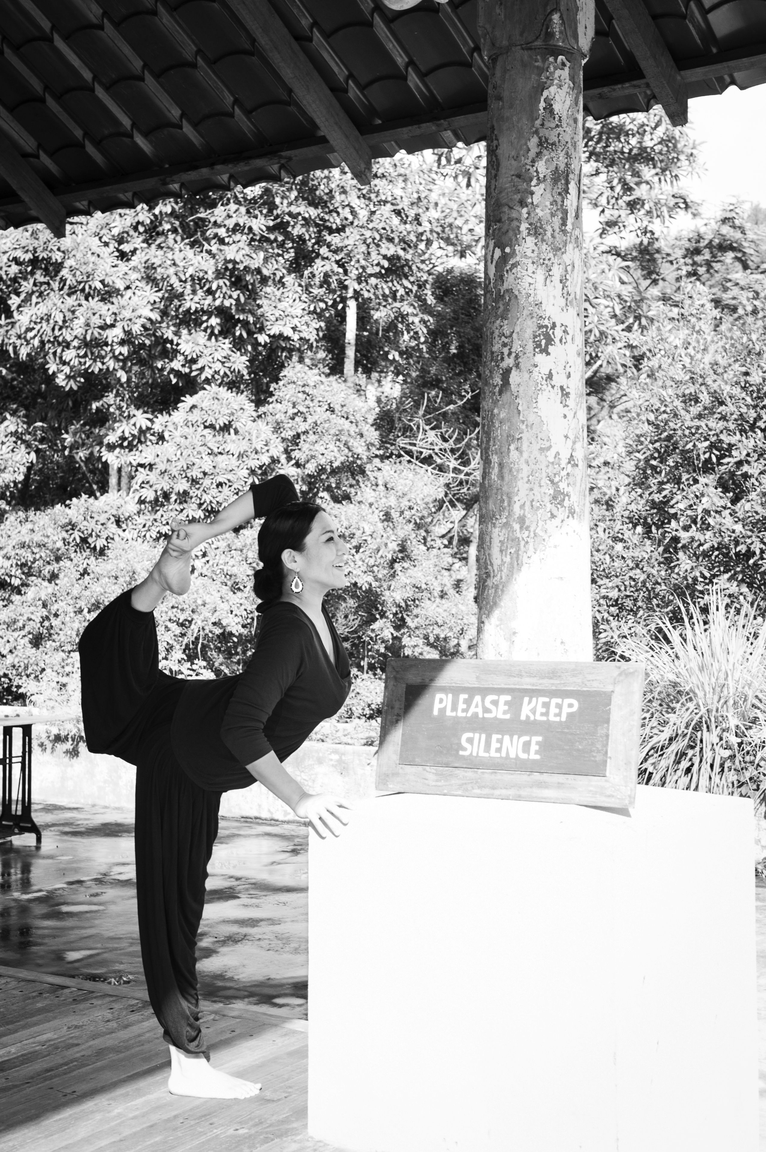 A person performing a yoga pose outdoors with a 'Please Keep Silence' sign in the foreground.