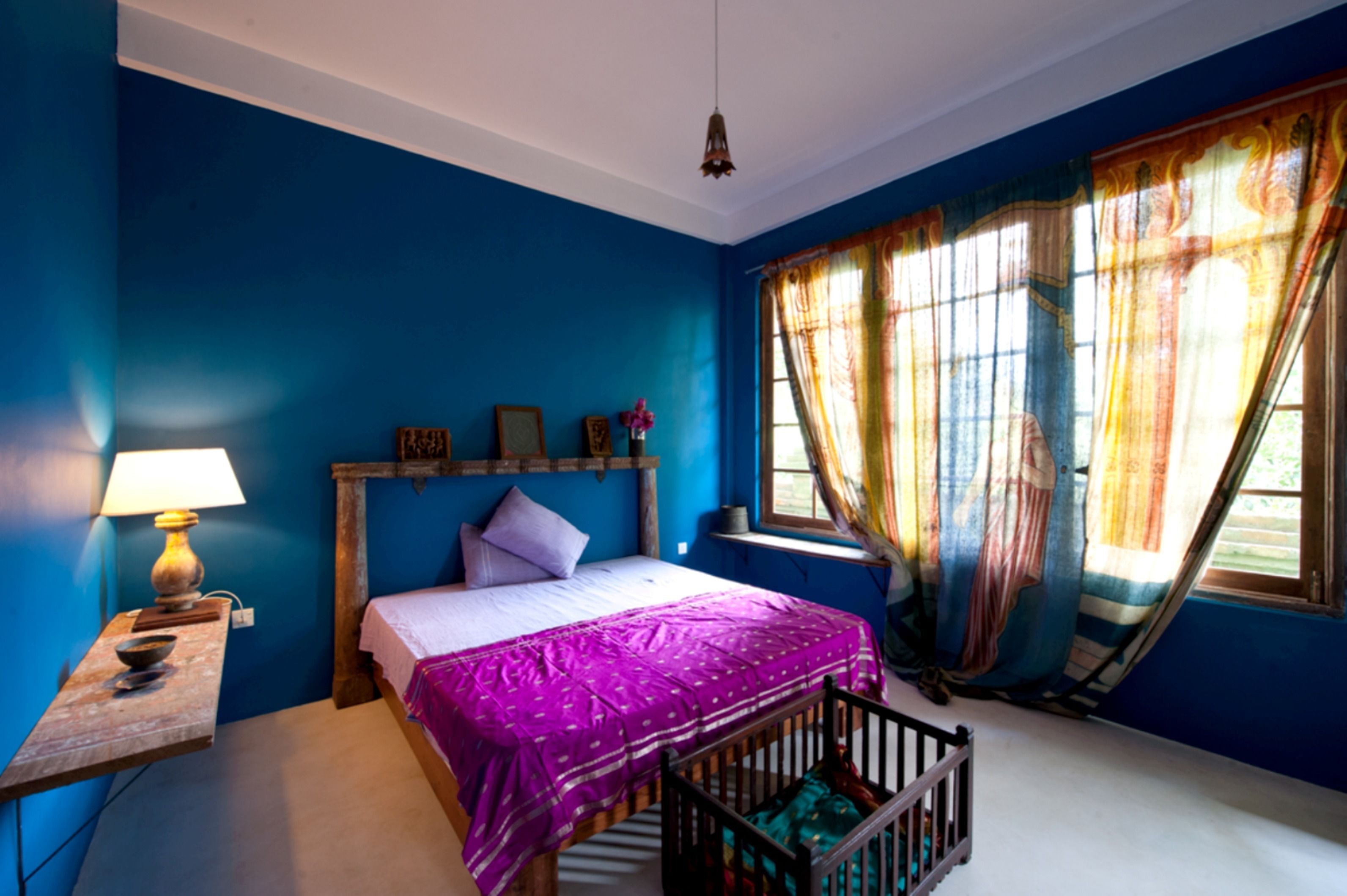 A bedroom with a bed, a crib, a nightstand, and a window with curtains.