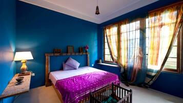 A bedroom with a bed, a crib, a nightstand, and a window with curtains.