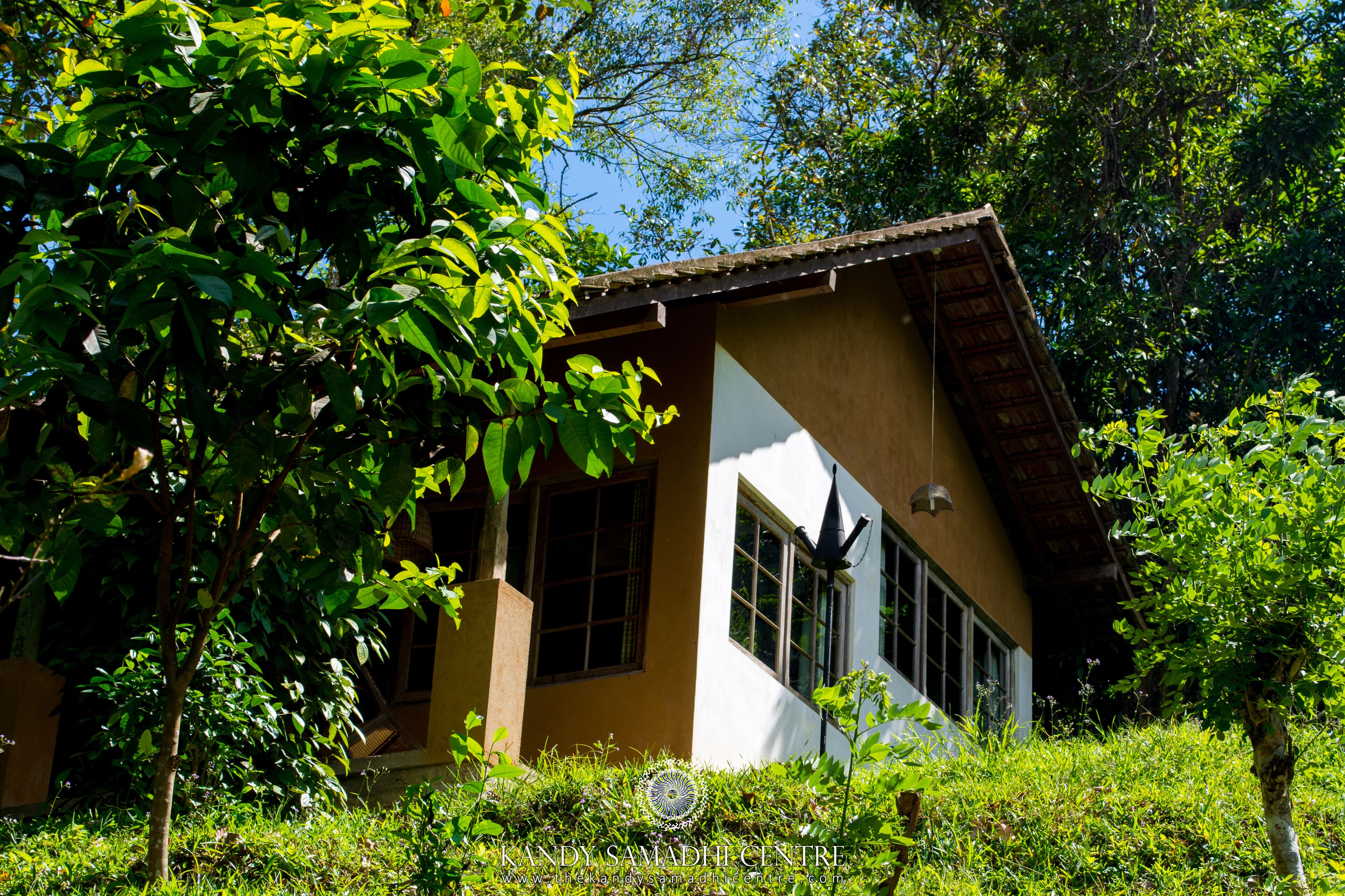 A building with a sloped roof and large windows, surrounded by lush greenery.