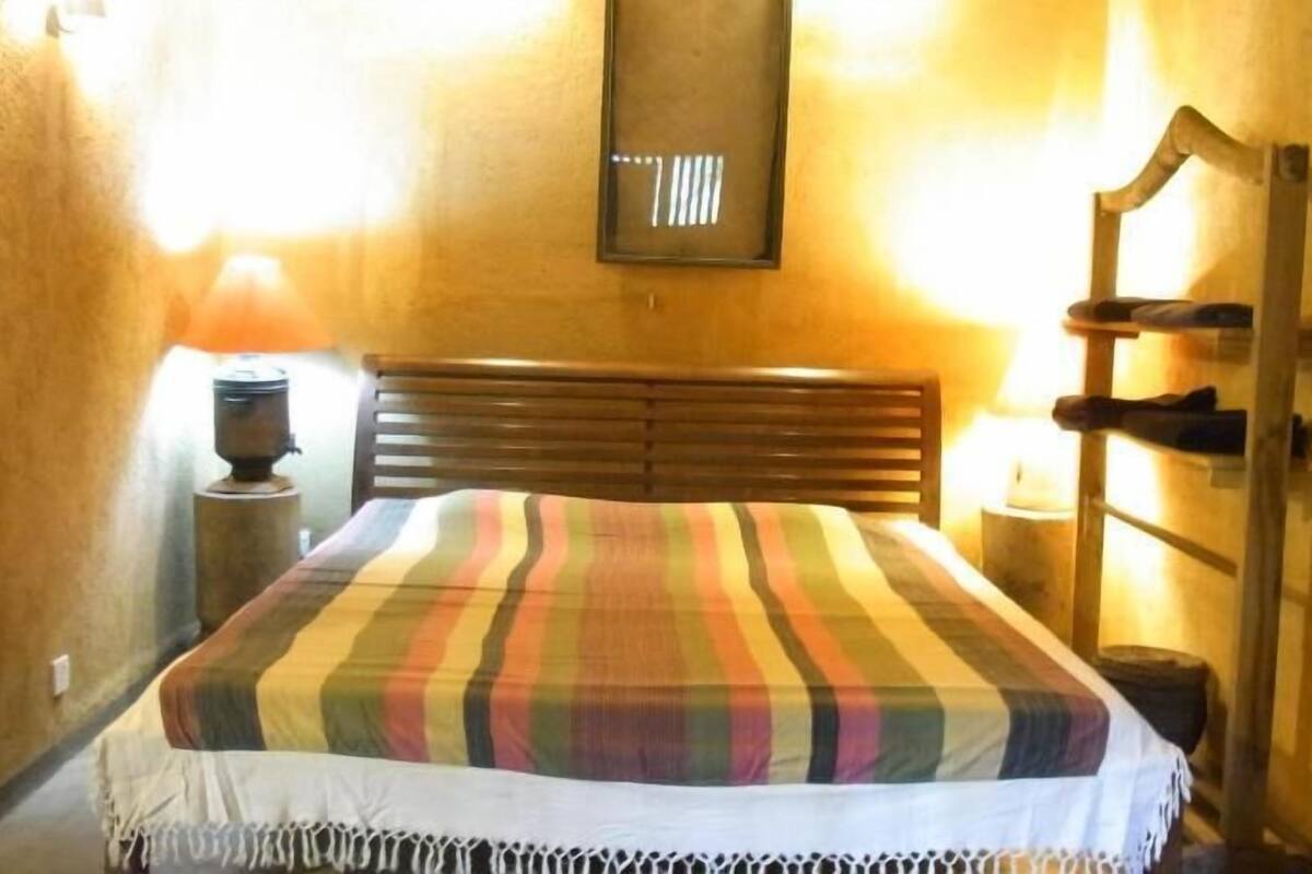 A room with a bed, a wooden headboard, a wall-mounted light fixture, and a nightstand with a lamp.