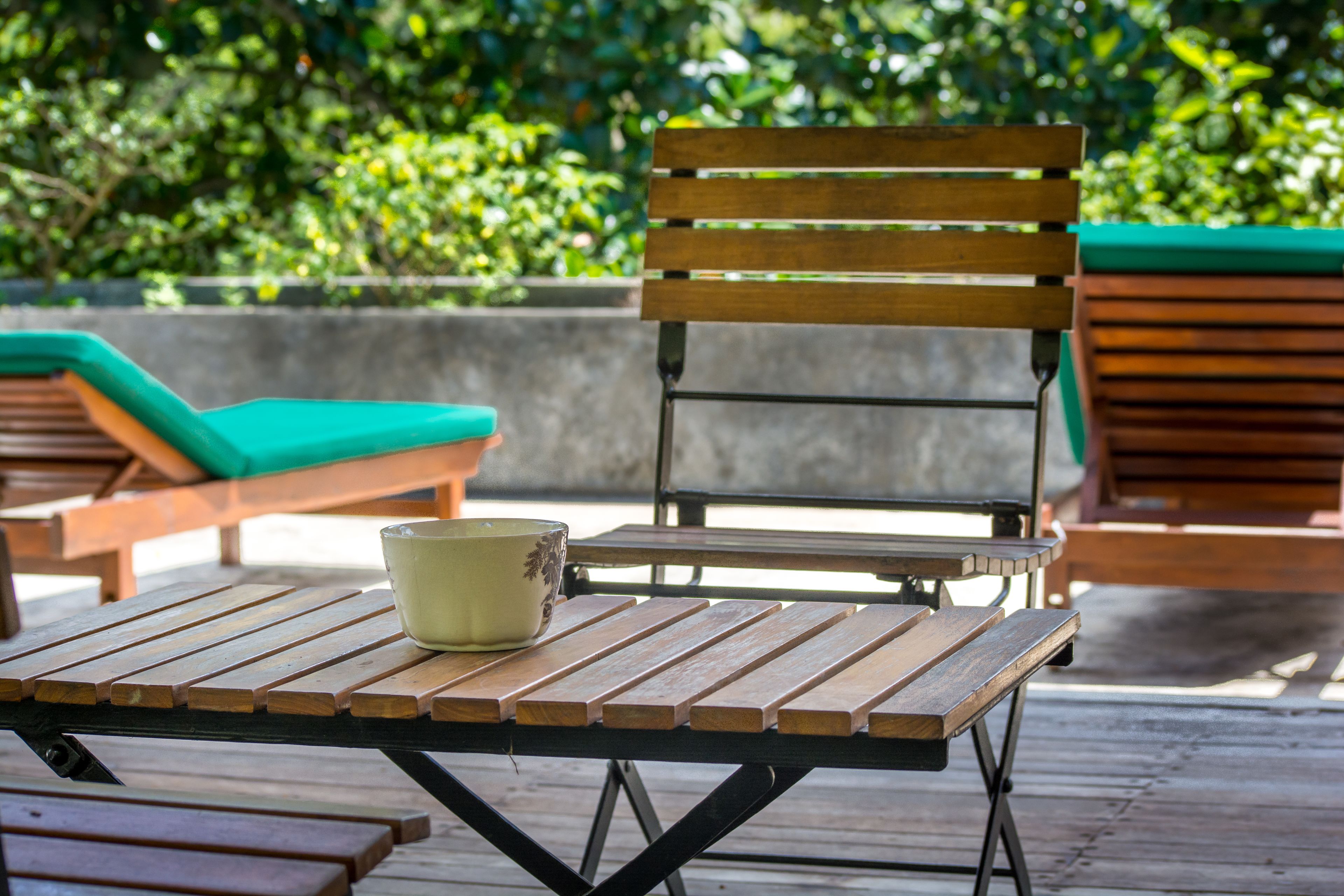 A wooden bench with a green cushion and a ceramic bowl on a wooden table.