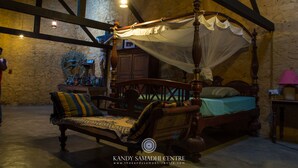 A traditional four-poster bed with a canopy, a wooden bench with cushions, and a stone wall in the background. - The Kandy Samadhi Centre (Kundasale)