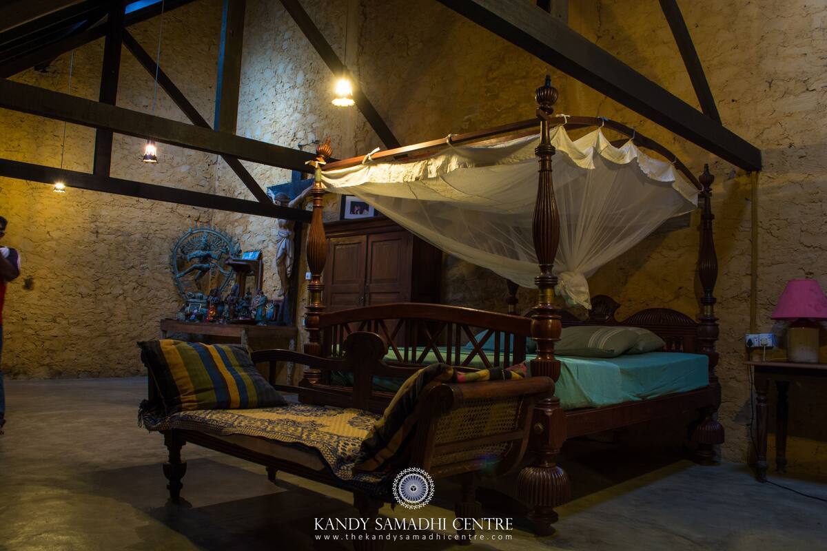 A traditional four-poster bed with a canopy, a wooden bench with cushions, and a stone wall in the background.