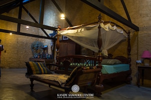 Uma cama de dossel tradicional com cortinas, um banco de madeira com almofadas e uma parede de pedra ao fundo.