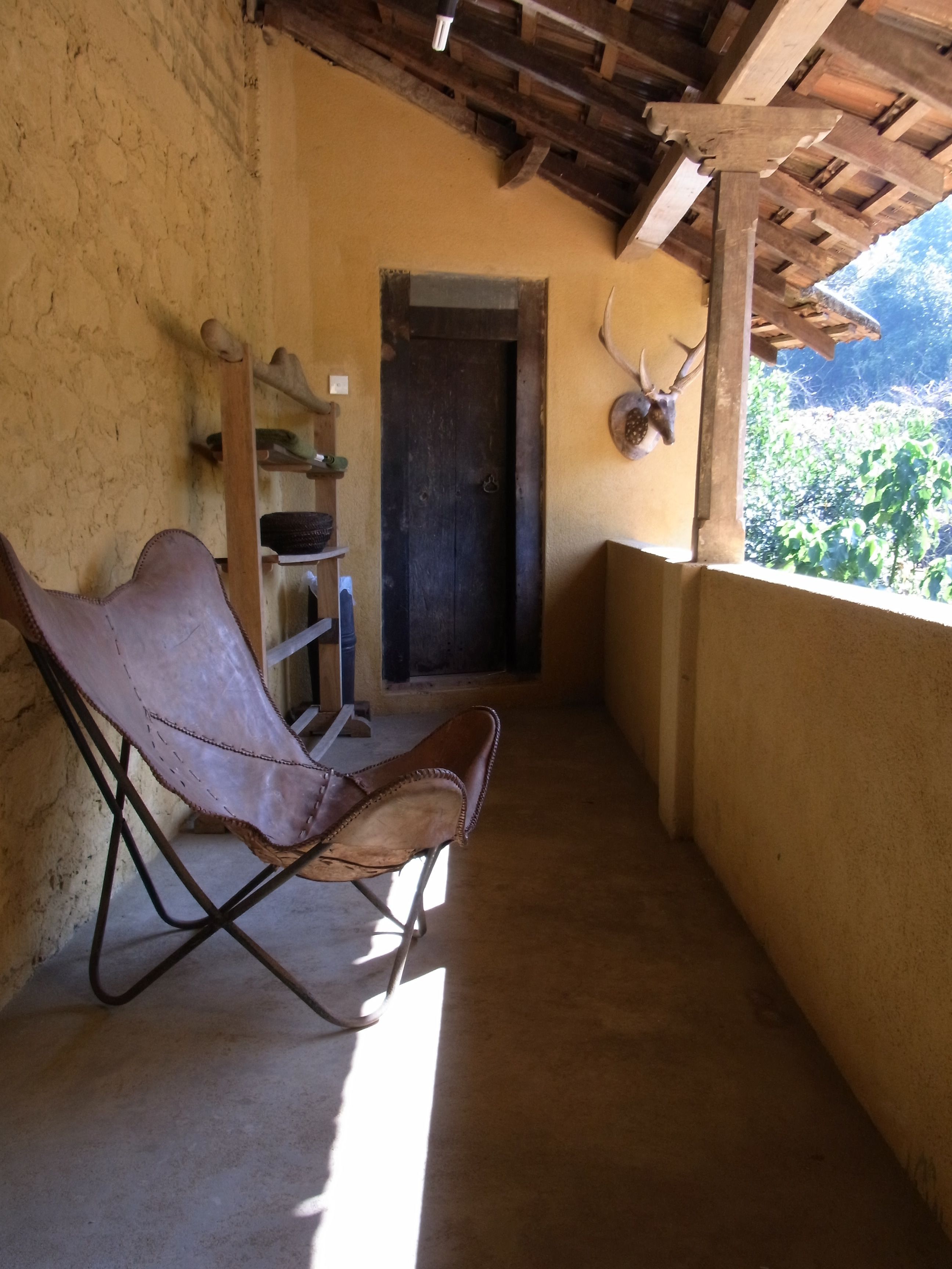 A rustic wooden chair in a narrow corridor with a wooden door and shelves against the wall.