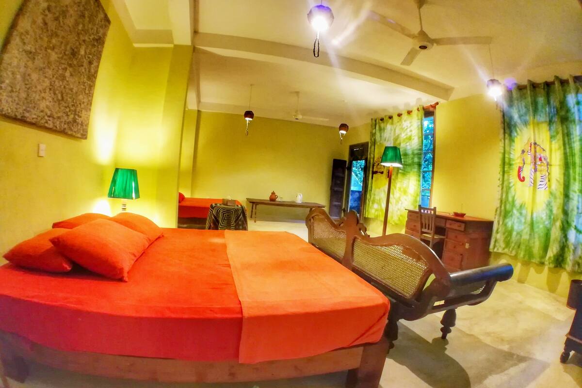 A bedroom with a large bed, a desk, a chair, and a ceiling fan.