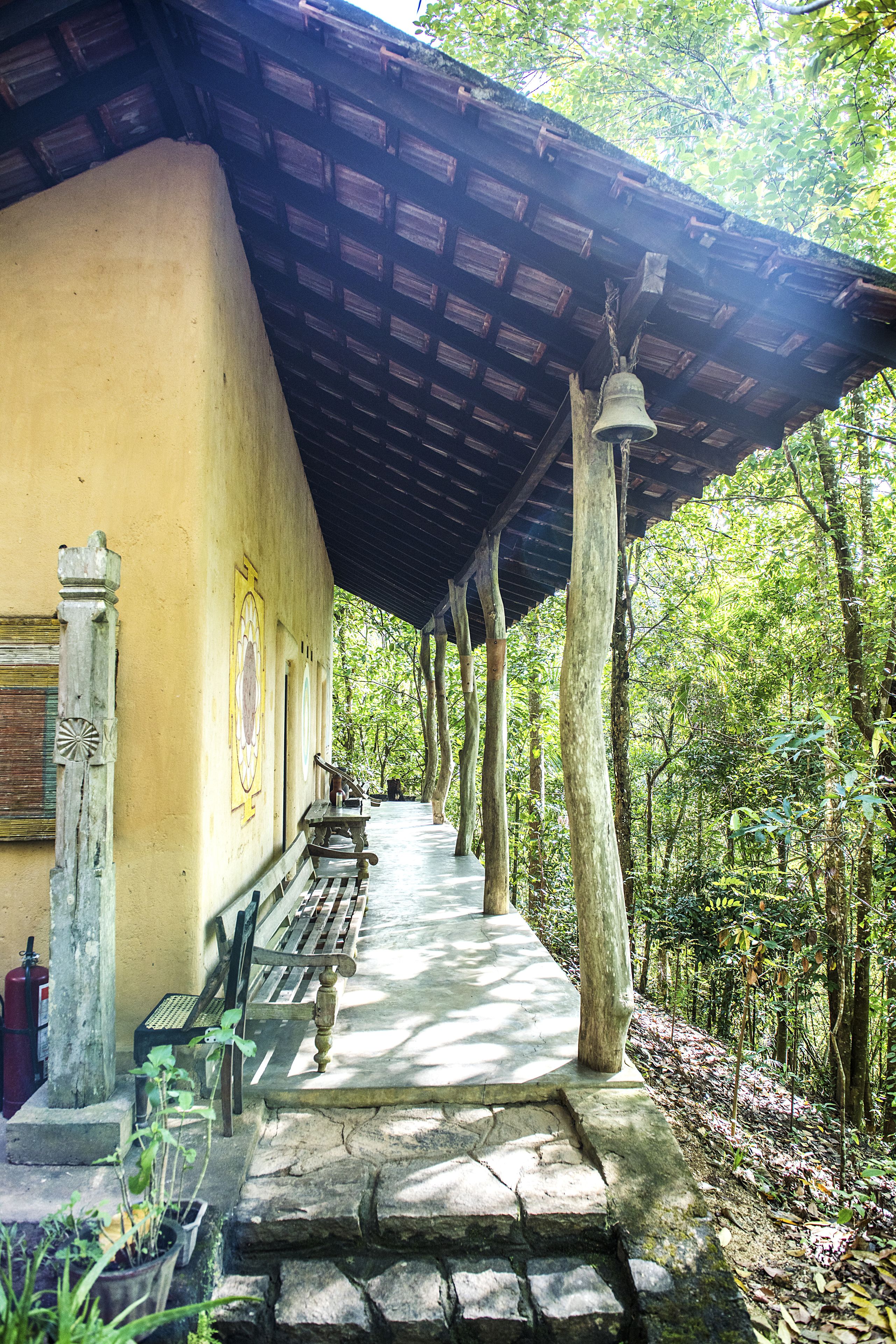 A covered outdoor area with benches, a stone pathway, and a bell hanging from a wooden post.