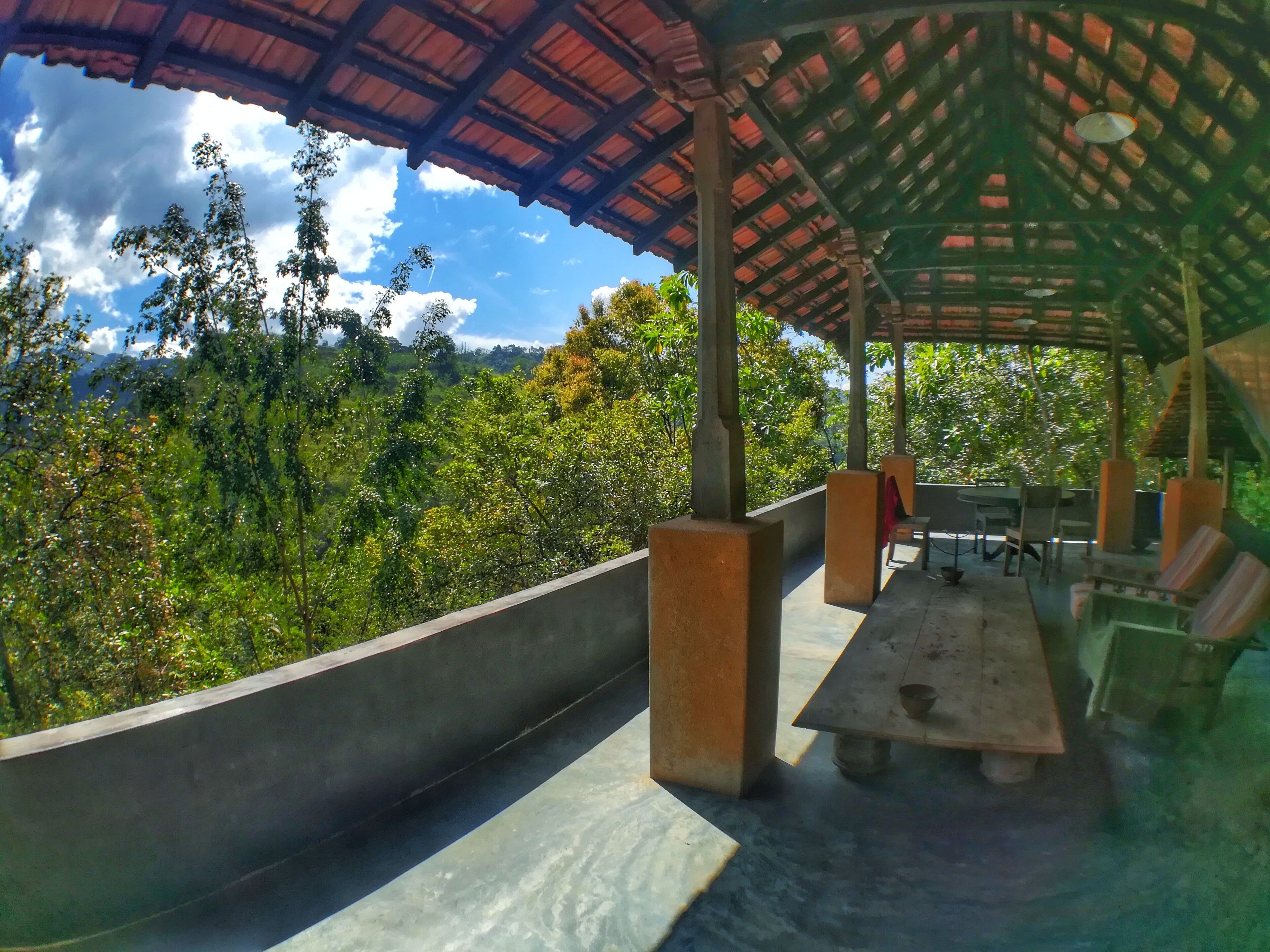 An outdoor seating area with a table and chairs, surrounded by a concrete wall and a metal roof structure.