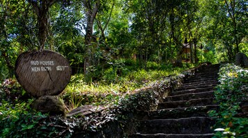 Uma placa de madeira com texto, uma escadaria de pedra e vegetação exuberante.