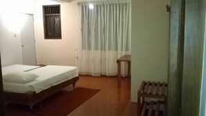 Une petite pièce simple, avec un lit simple, une chaise en bois, une petite table et une fenêtre avec des rideaux.