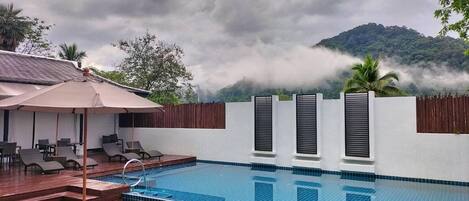 Una piscina con cubierta de madera, sillones de descanso y vistas a una cordillera.