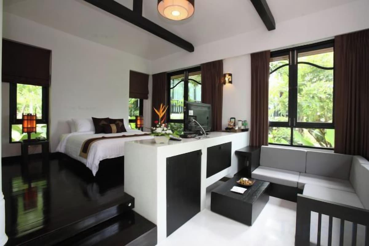 A modern hotel room with a bed, a sofa, a coffee table, and a TV.
