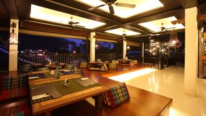 Un espacio interior amplio con una gran mesa de madera, varios arreglos de asientos, ventiladores de techo e iluminación colgante.