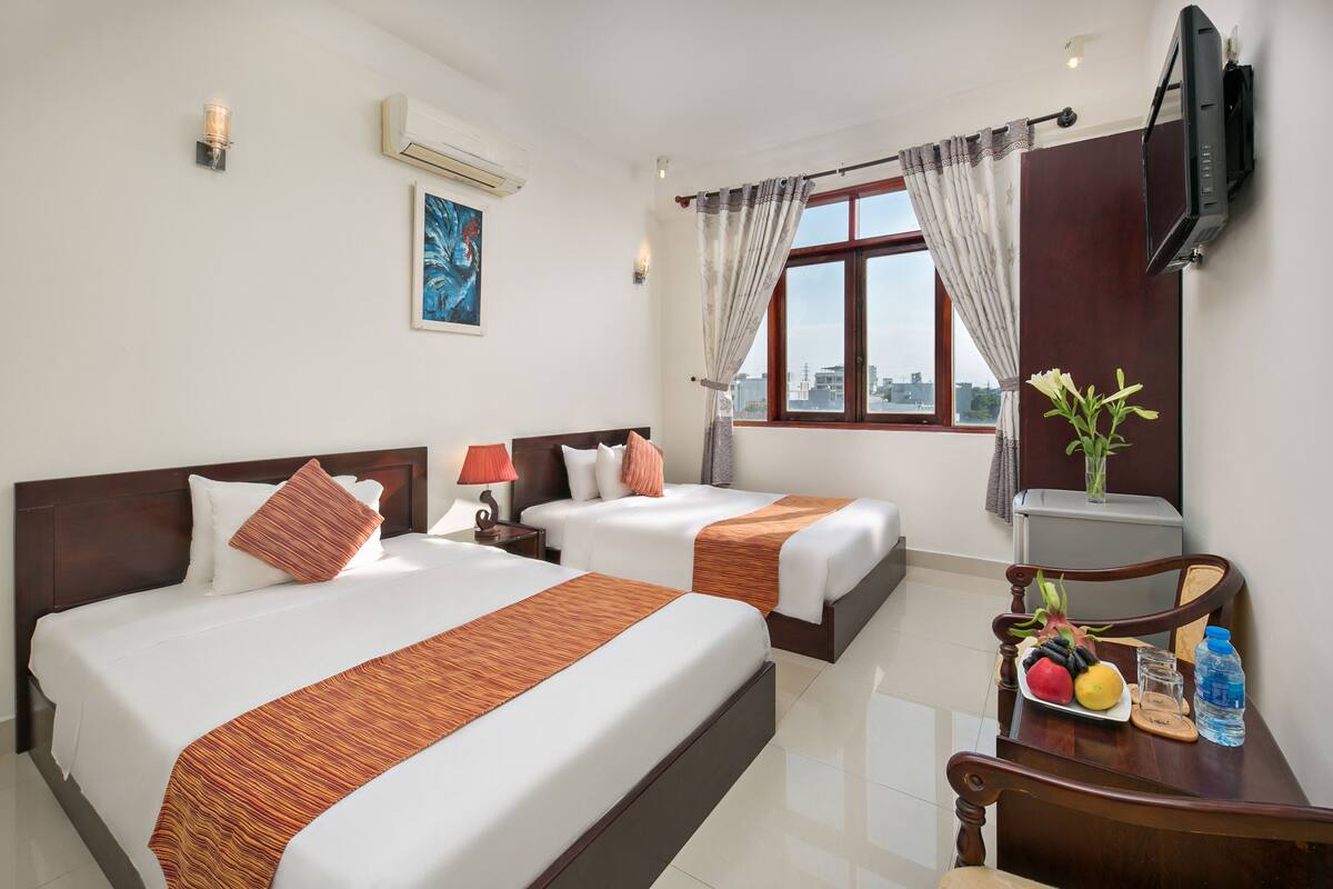 A hotel room with two beds, a TV, a desk with a chair, a window with curtains, and a city view.