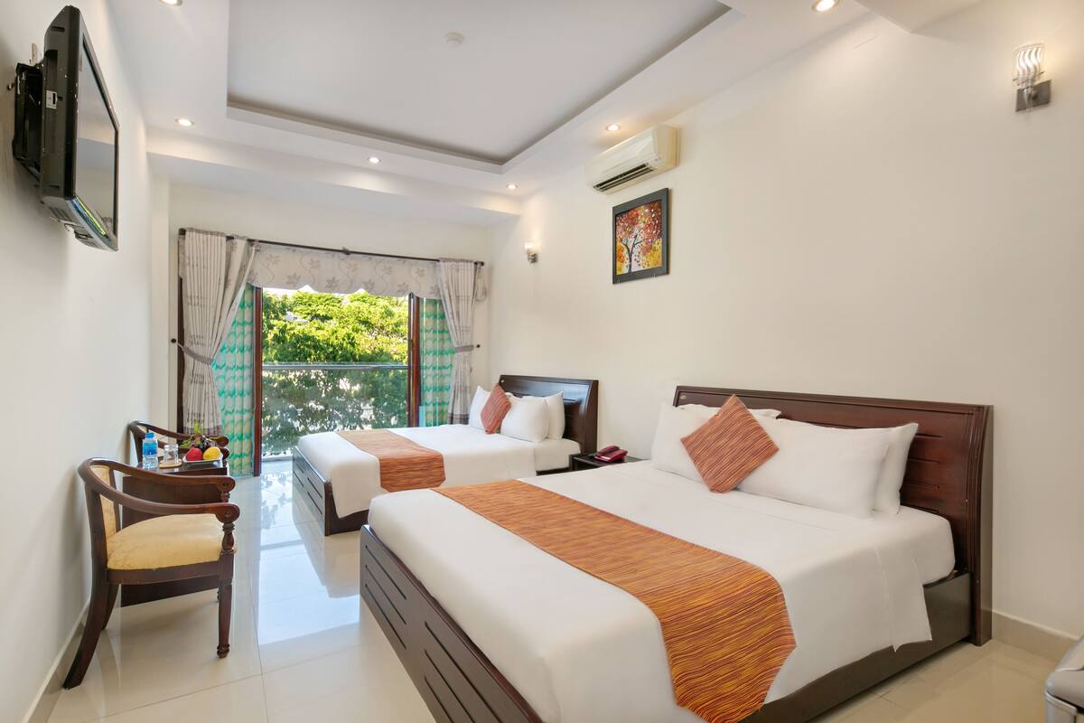 A hotel room with two beds, a TV, a desk with a chair, and a window with curtains.