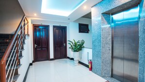 A modern interior with a staircase, two wooden doors, a potted plant, a fire extinguisher, and a metallic elevator. - Dreams Hotel Danang (Da Nang)