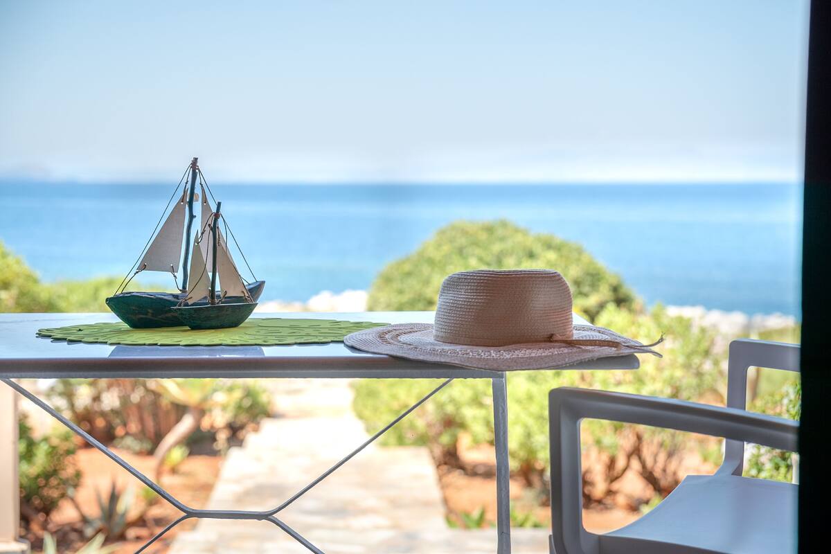 A table with a model sailboat and a straw hat on a balcony overlooking a scenic view.