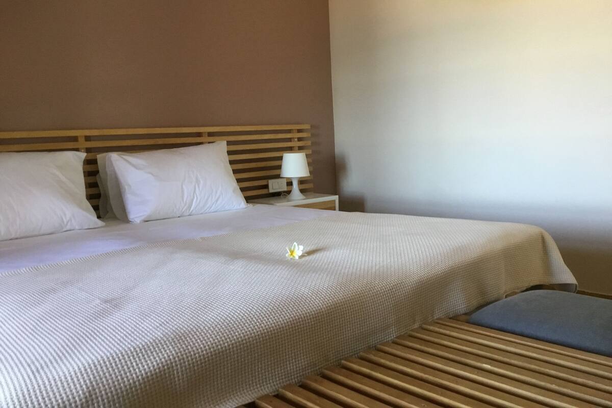 A neatly made bed with white linens, a wooden headboard, and a bedside table with a lamp.