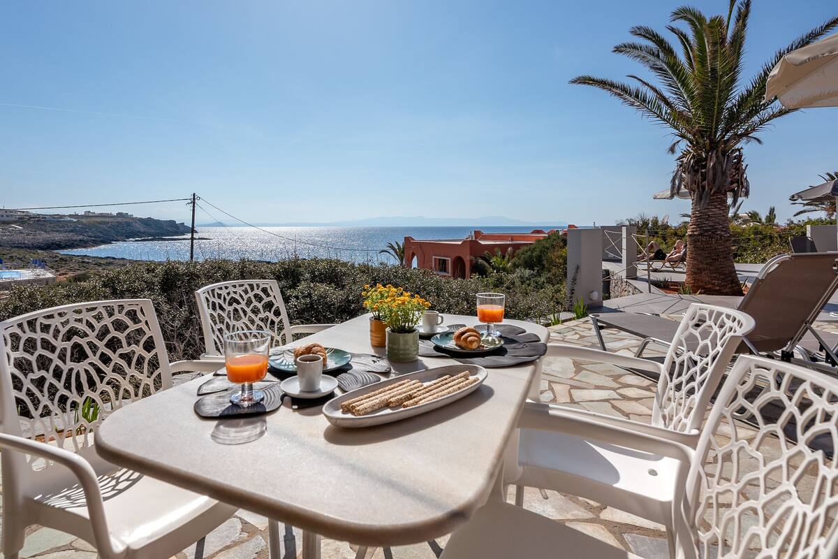 An outdoor dining area with a table set for two, overlooking a scenic coastal view.