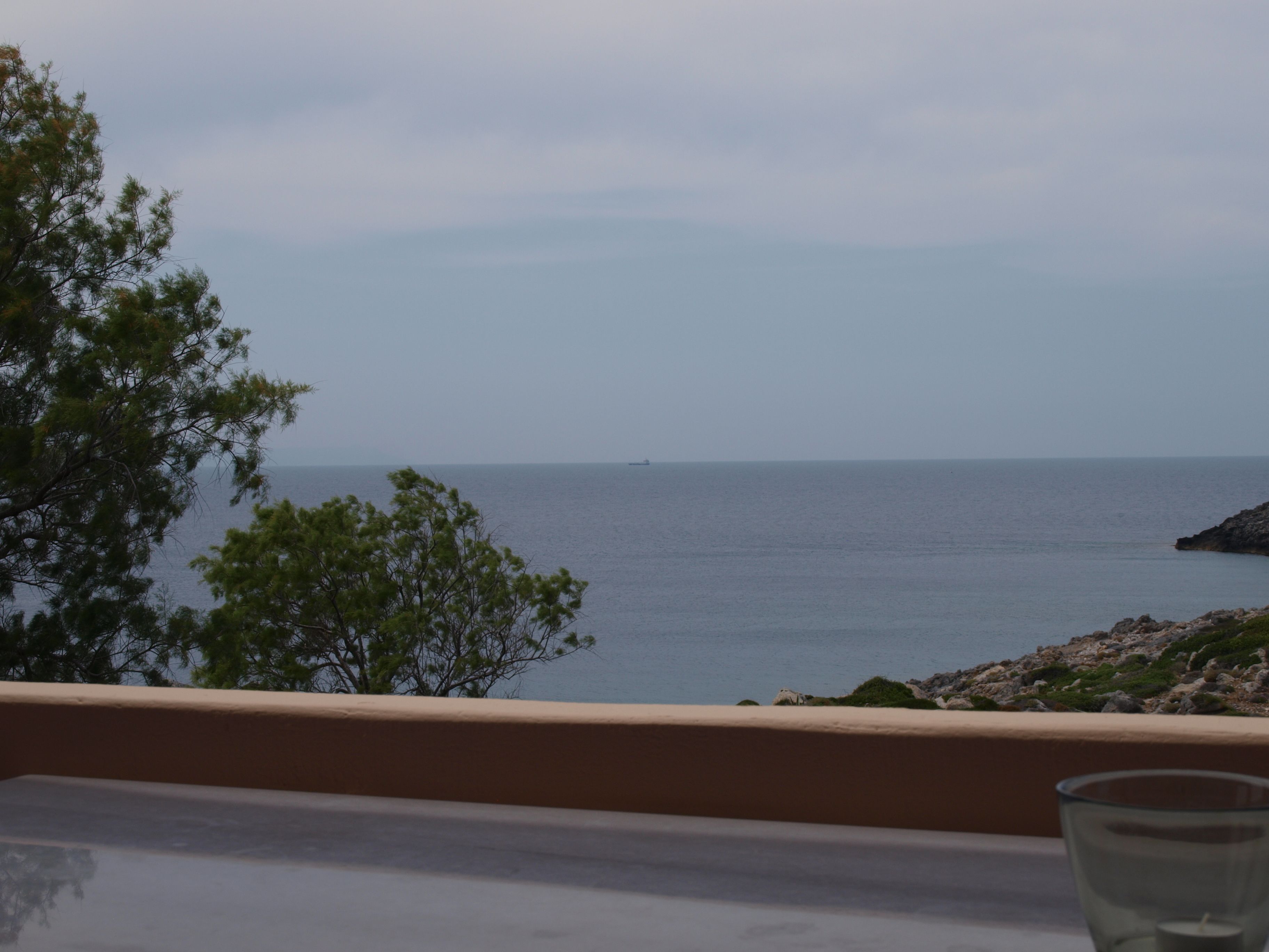 A balcony with a view of the sea and distant ship.