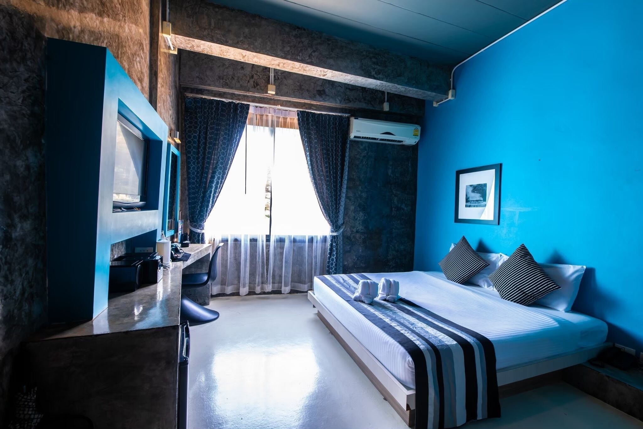 A bedroom with a bed, a desk, and an air conditioning unit.