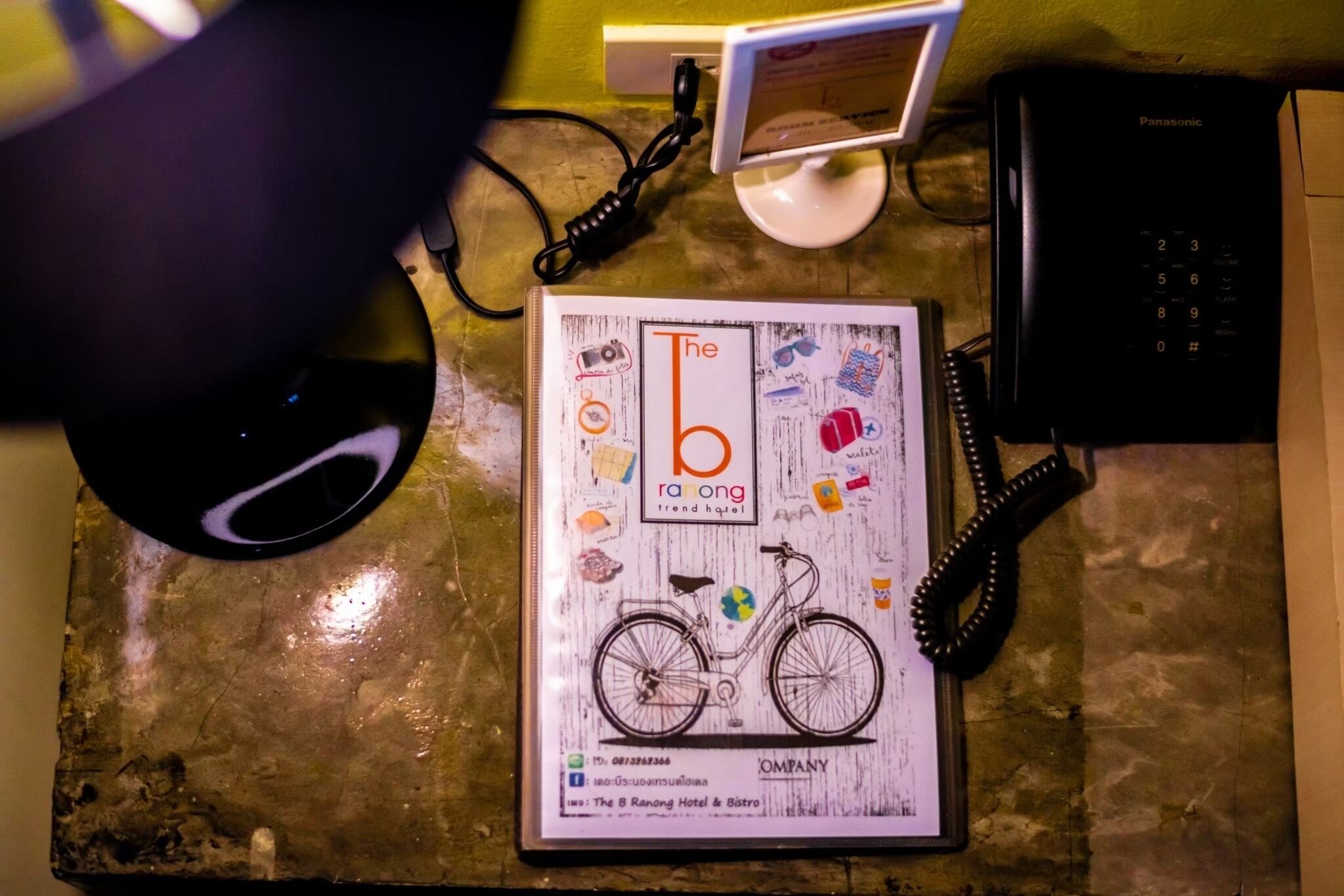 Uma mesa com uma revista emoldurada, um telefone e um abajur.