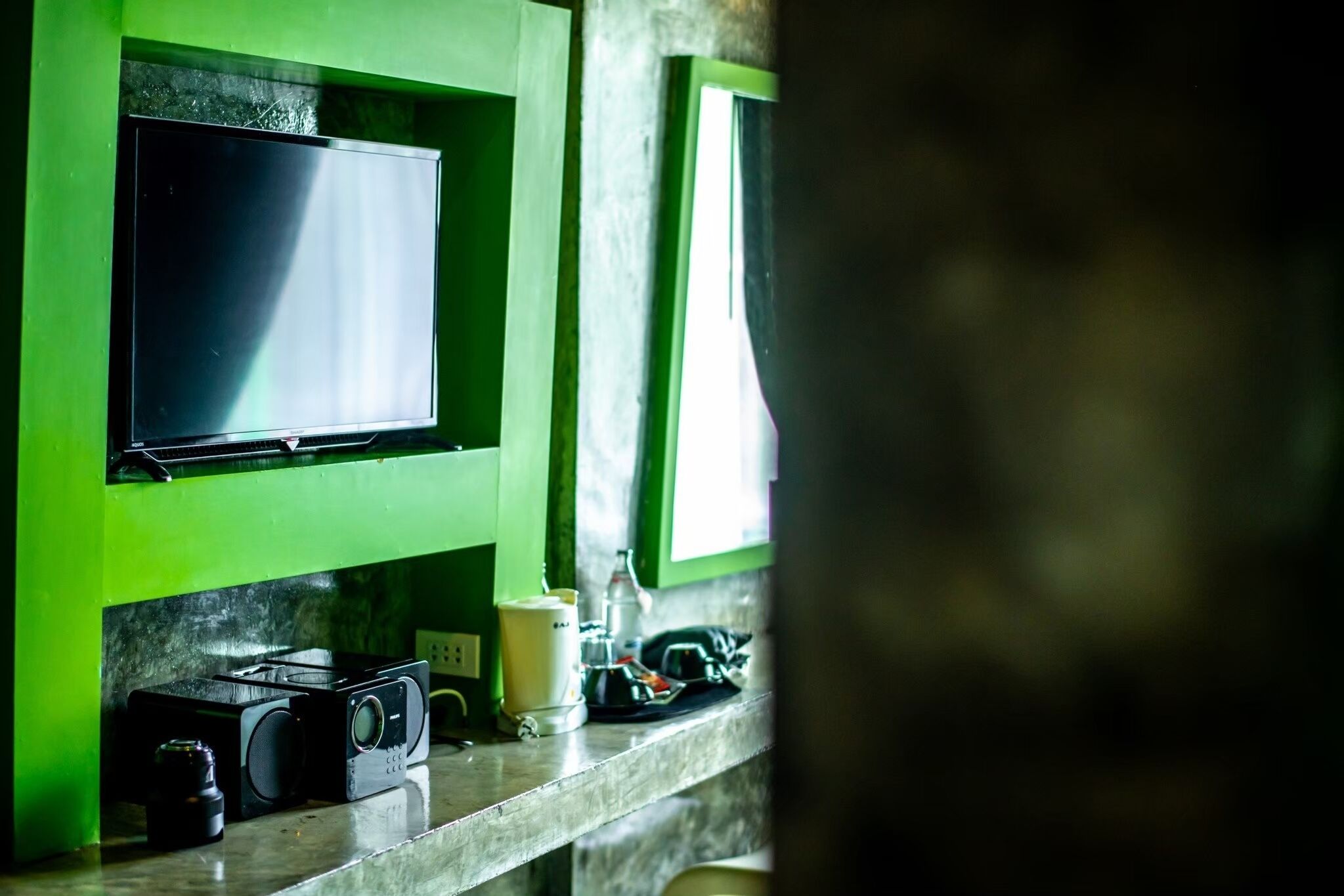 Una cuina amb taulell verd, una cafetera i un televisor fixat a la paret.